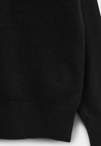 Pulover negru tricotat, cu o textură moale, manșete și tiv cu dungi. Materialul pare gros, cu o finisare netedă.