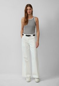 Top sin mangas a rayas combinado con pantalones anchos de tiro alto blancos y un cinturón negro. El conjunto presenta un corte relajado y zapatillas casuales.