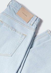 Jeans de mezclilla azul claro, con corte recto, una etiqueta de marca de cuero en la parte de atrás y costuras amarillas contrastantes.