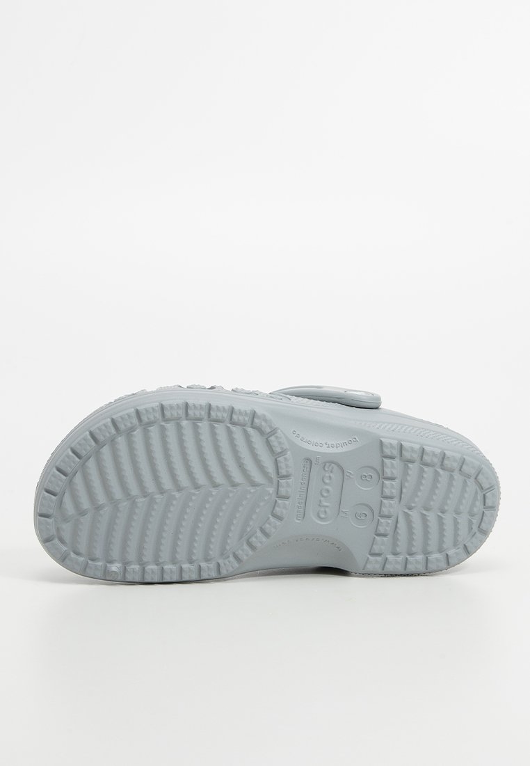 Suela de zapato Crocs de color gris claro con un patrón texturizado y estriado para mayor tracción. Presenta detalles de logotipo en relieve y marcas de tamaño de pie.