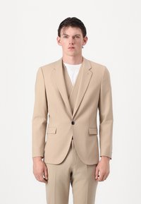 Completo beige composto da un giubbotto sartoriale con revers a V e pantaloni abbinati, realizzato in tessuto liscio con una sottile texture.