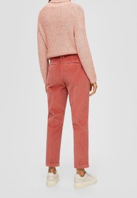 Vaaleanpunainen ribbikuvioitu neulepaita, joka on yhdistetty korallinvärisiin samettimekkoihin, joissa on rento leikkaus ja joustava vyötärö. Jalkineina vaaleat lenkkarit.