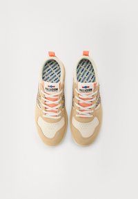 Beige sneakers med hvite detaljer, med teksturert overdrev, fargerike lisser og mønstret såle. Pull-tab ved hælen for enkel påkledning.