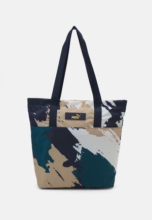 Sac cabas avec motif abstrait en coups de pinceau bleu marine, beige, blanc et sarcelle, avec des anses noires et un patch logo Puma à l'avant.
