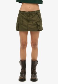 Schip kledinggroen cargorok met knoopsluiting, twee voorzakken en zijzakken. Draag met zwarte leren enkellaarzen.