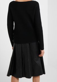 Pull en maille côtelée noire au design dénudé d'épaules, associé à une jupe évasée en simili cuir noir présentant des coutures visibles et une texture lisse.