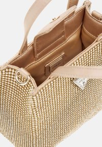 Borsa con perline dorate, con un interno beige liscio, caratterizzata da un'etichetta con marchio e doppi manici superiori per una facile portabilità.