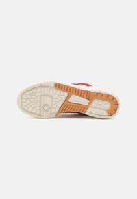 Zdravotná obuv Adidas s podrážkou v off-white gumovom vyhotovení s textúrovaným gripom, ktorá obsahuje oranžový akcent a geometrický dezén pre lepšiu trakciu.