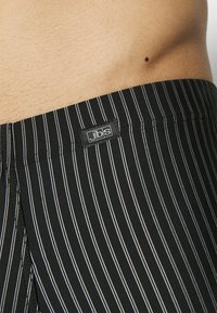 Zwart-witte gestreepte tailleband van de onderbroek met een klein zwart label waarop "jbs." staat. De stof lijkt zacht en elastisch.