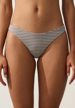 Frau trägt Bikinihose mit niedrigem Bund und dünnen horizontalen schwarz-weißen Streifen, zeigt Torso und obere Oberschenkel.