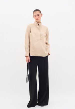 Beige collared shirt with a front placket, paired with wide black trousers. The outfit features a smooth texture and a minimalist design.