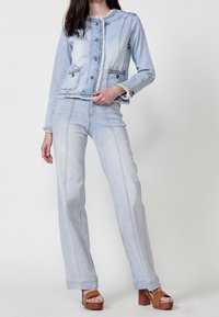 Light blue denim jacket with braided trim and buttons, paired with matching flared jeans featuring center seams and a soft texture.