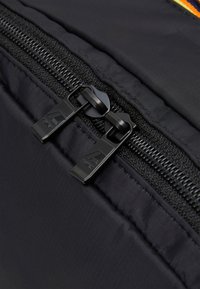 Zip de sac à dos en nylon noir avec deux tirettes noires, présentant une texture lisse et un branding minimal sur les tirettes métalliques.