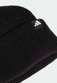 Black ribbed knit beanie with folded cuff and small black tag featuring a white Adidas logo on light gray background.