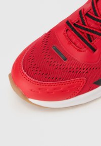 Κόκκινο αθλητικό παπούτσι με πάνω μέρος από δίχτυ, μαύρα κορδόνια και λαστιχένια σόλα με υφή και αεριζόμενες επιφάνειες για καλύτερο αερισμό.