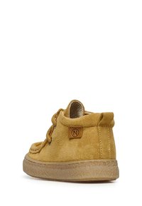 Stivaletto giallo in suede con punta tonda, lacci frontali e morbida fodera interna. Presenta una suola in gomma texturizzata e un piccolo tag con logo.