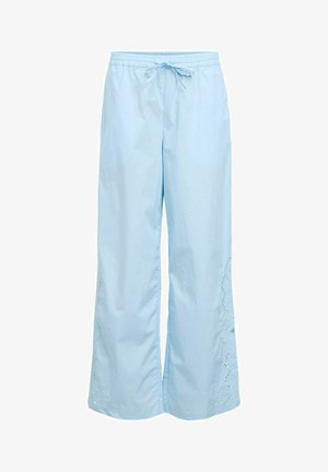 Pantalon ample bleu clair avec taille élastique et cordon de serrage, présentant des détails en dentelle découpée le long de la partie inférieure externe des jambes.
