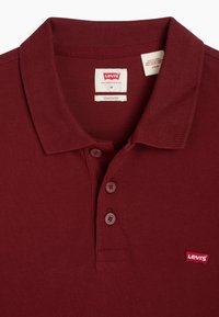 Polo en bordeaux en coton texturé, avec une patte de boutonnage à deux boutons et un petit logo Levi's rouge sur la poitrine gauche.