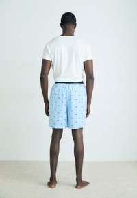 Light blue cotton shorts with small black patterns, elastic waistband, and a relaxed fit. Paired with a white short-sleeve t-shirt.