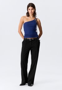 Μπλε ναυτικό τοπ με έναν ώμο και λεπτομέρειες κουμπιών στο πλάι, σε συνδυασμό με μαύρο παντελόνι φαρδιάς γραμμής και κομψά παπούτσια. Μινιμαλιστικός σχεδιασμός και εφαρμοστή γραμμή.