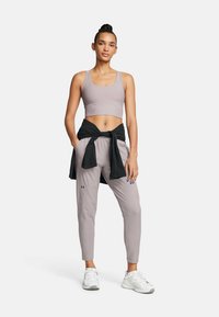 Lichtgrijze sportoutfit met een geribde crop top en taps toelopende broek, met een zwarte jas om de taille gebonden. Witte sneakers maken de look compleet.