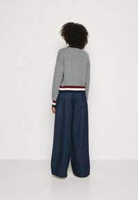 Grauer Strickpullover mit gestreiftem Saum und navyblauen weit geschnittenen Jeans. Das Outfit verfügt über gerippte Bündchen und eine lockere Passform.