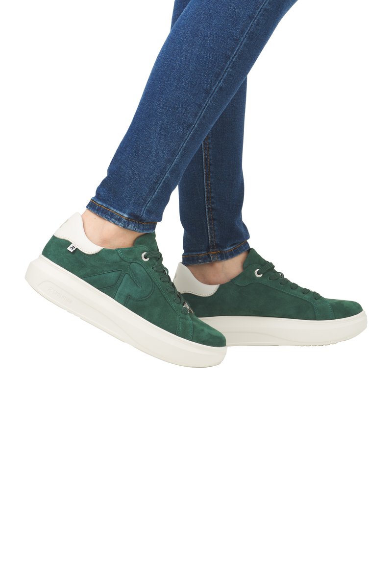 Green suede sneakers with white accents, round toe, lace-up design, and a textured white sole; viewed from the side with denim pants.