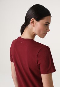 T-shirt in cotone bordeaux con maniche corte, scollatura rotonda e dettagli cuciti sulla spalla. Texture liscia, design semplice.