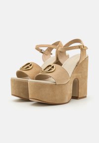 Sandales à plateforme en suède beige avec un épais talon carré et une sangle de cheville. Présente un bijou de boucle dorée sur la sangle des orteils.