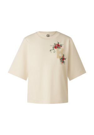 Jasnobeżowa koszulka z krótkimi rękawami, ozdobiona kwiatowym haftem w kolorze czerwonym i zielonym oraz wyraźnym wzorem litery "B" na przodzie.