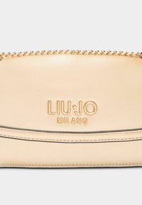 Kožená peněženka v tan barvě s pozlaceným zipem na řetízku, embosovaným logem a zakřivenými švy pro přidanou texturu.