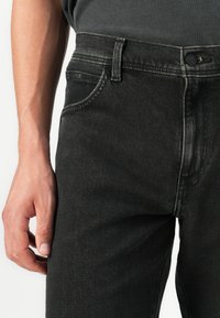 Mustadest denimist teksad sirge lõikega, klassikalise viie tasku disainiga ja minimalistlike õmbluste detailidega. Nööbiga sulgemine taljes.
