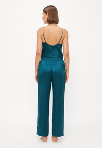 Teal sateng loungewear-set som består av en ermeløs topp med tynne stropper og vide bukser med elastisk liv, glatt tekstur.