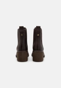 Botas de cuero marrón hasta el tobillo con un tacón de bloque, que presentan costuras laterales y bucles de agarre, textura suave y diseño de punta redondeada.