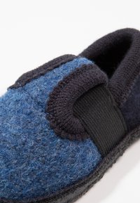 Blaue Filzschlappen mit einem schwarzen elastischen Riemen und einer kontrastierenden dunklen Sohle. Die Textur ist weich, mit einem abgerundeten, lässigen Design.