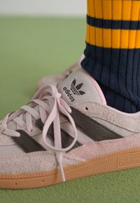 Ροζ σουέτ αθλητικά παπούτσια με γκρι δερμάτινες ρίγες και ροζ κορδόνια. Διαθέτουν ανάγλυφο λογότυπο και σόλα από καουτσούκ γόμας. Φοριούνται με σκούρες μπλε ριγέ κάλτσες.