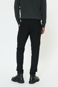 Juodos kelnės siauru siluetu, pagamintos iš lygaus audinio. Dvi kišenės gale su sagų užsegimu. Derinamos su tvirtais juodais batais.