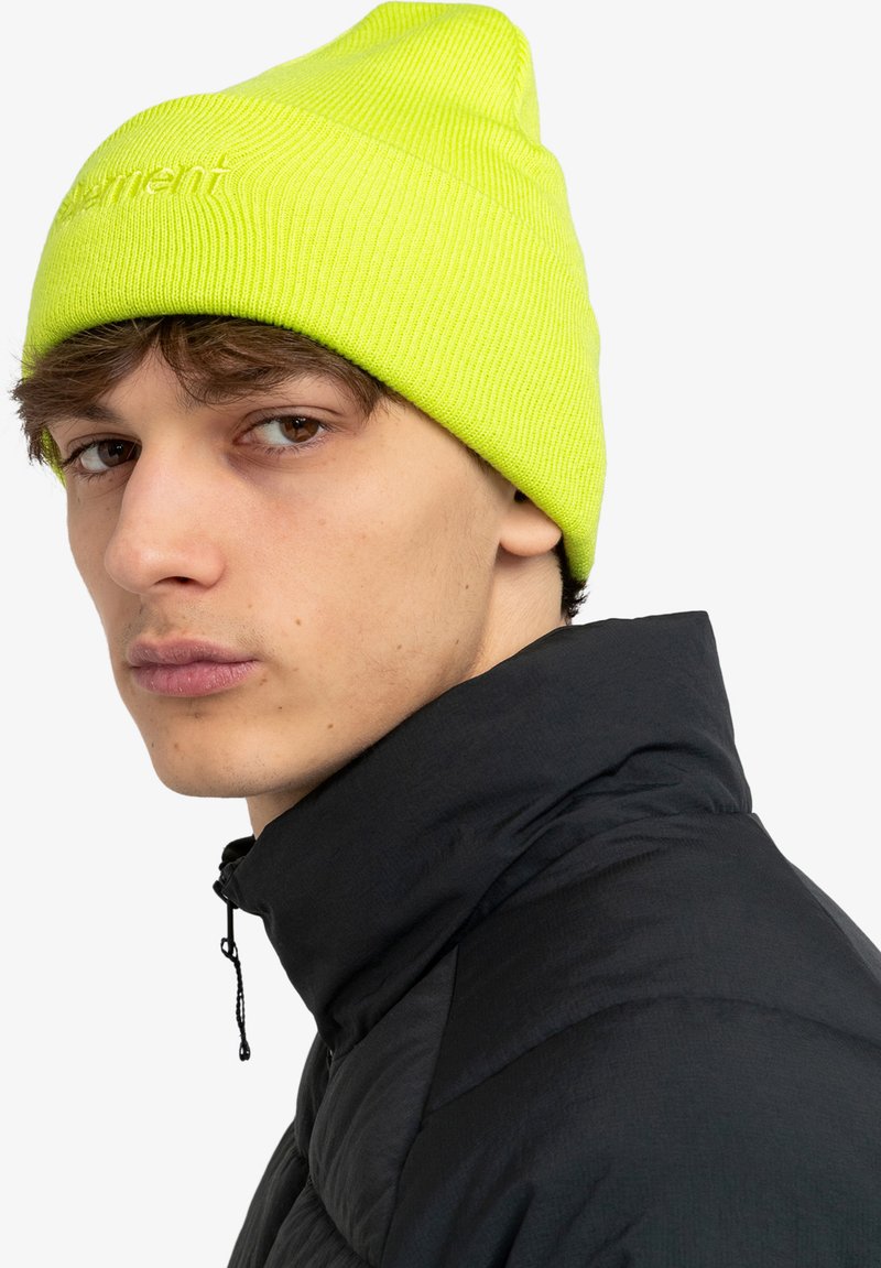 Beanie a coste giallo neon con una vestibilità aderente. Indossato con un giubbotto imbottito nero con colletto alto e dettagli con cerniera.