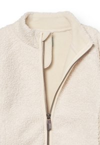 Cremefarbene Fleecejacke mit hohem Kragen, durchgehendem Reißverschluss und weicher Innenseite. Auffällige strukturierte Außenseite mit glattem Reißverschluss-Zipper.