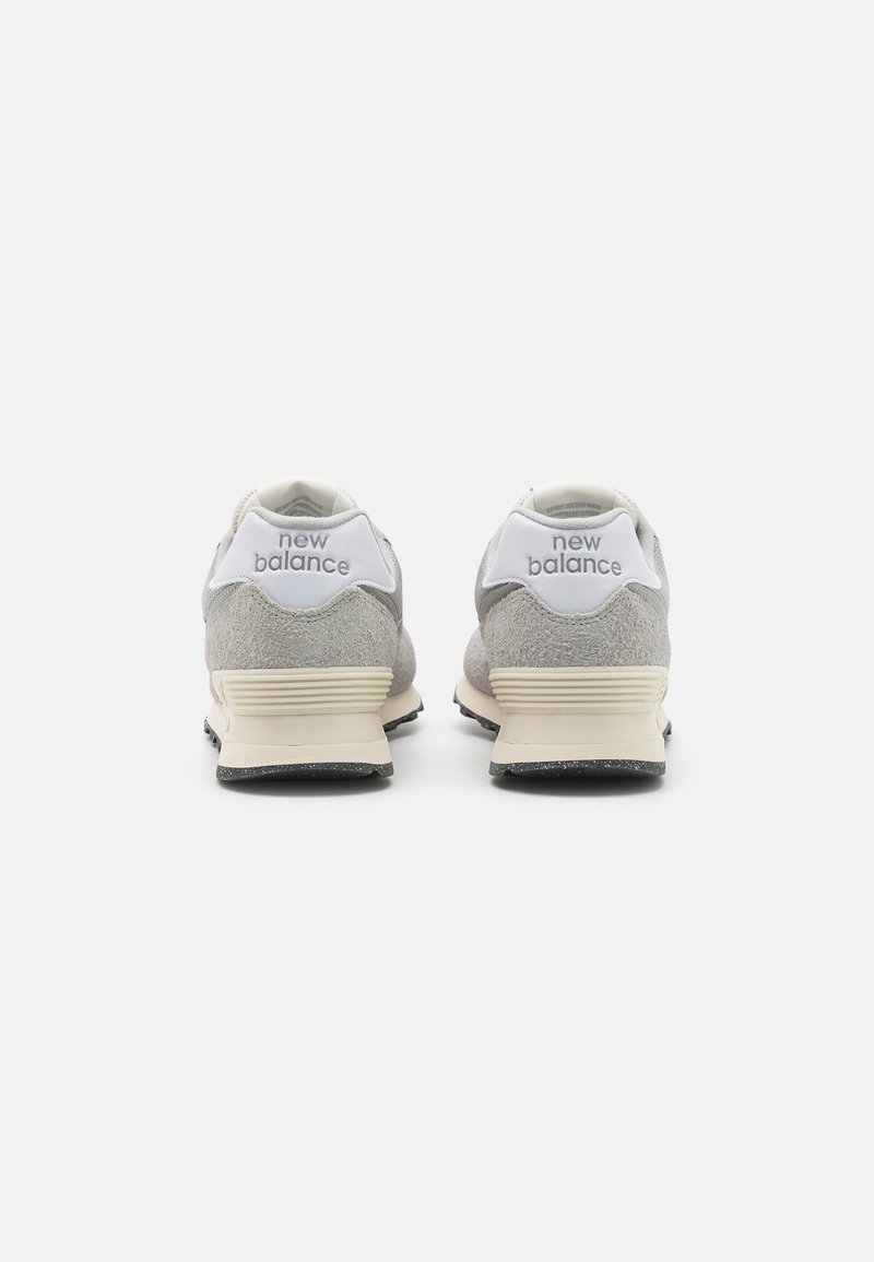 Graue Wildleder- und weiße Leder-Sneaker mit runden Rückseiten, schwarzer Sohle und "New Balance"-Branding an der Ferse. Minimalistisches Design.
