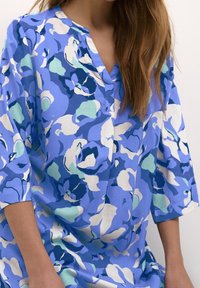 Blumen-Tunika in Blautönen, mit V-Ausschnitt, Dreiviertelärmeln und lockerer Passform. Aus leichtem Stoff mit einer sanften Textur gefertigt.