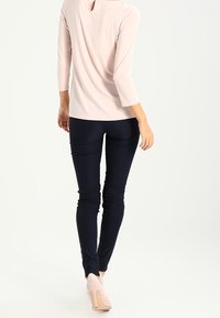 Světle růžový top s detailem na zádech ve tvaru klíčové dírky, tříčtvrteční rukávy, spárovaný s tmavě modrými slim-fit kalhotami a světle růžovými lodičkami.