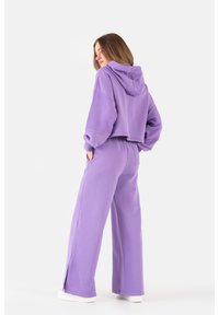 Przycięta purpurowa bluza z kapturem oraz szerokie purpurowe spodnie. Miękka faktura, luźny krój, z bocznymi rozcięciami u dołu spodni.