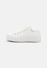 White sneaker with a smooth canvas upper, round toe, and textured rubber sole. Features metal eyelets and a subtle brand logo on the heel.