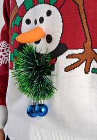 Sweter świąteczny z warkoczy z motywem bałwanka, pomarańczowym noskiem z pianki, zielonym detalem z bibuły i niebieskimi metalicznymi dzwoneczkami.