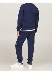 Granatowy sweter z okrągłym dekoltem i ściągaczami, w zestawie z zwężającymi się granatowymi dresami z logo. Białe trampki dopełniają stylizację.