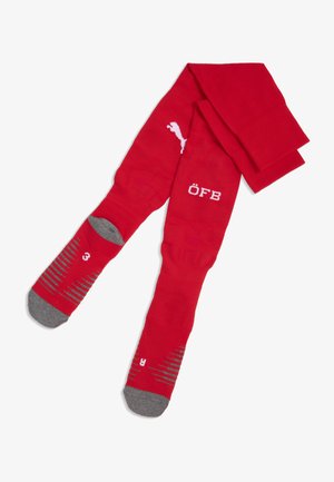 Calcetines deportivos rojos hechos de una tela elástica. Presentan detalles grises en la punta y el talón con patrones de rayas, y letras blancas "ÖFB".