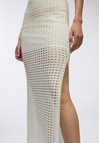 Gonna bianca all'uncinetto con uno spacco, caratterizzata da un motivo testurizzato di ritagli circolari. Il materiale ha una qualità trasparente ed un design aderente.