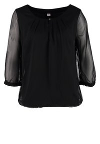 Blouse noire avec manches trois-quarts transparentes, encolure ronde, petit bouton frontal et plis subtils sous l'encolure.