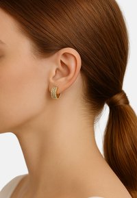 Goldene Creolen mit funkelnden Strasssteinen, die in drei horizontalen Reihen angeordnet sind, und ein geschwungenes Design sowie eine polierte Oberfläche aufweisen.